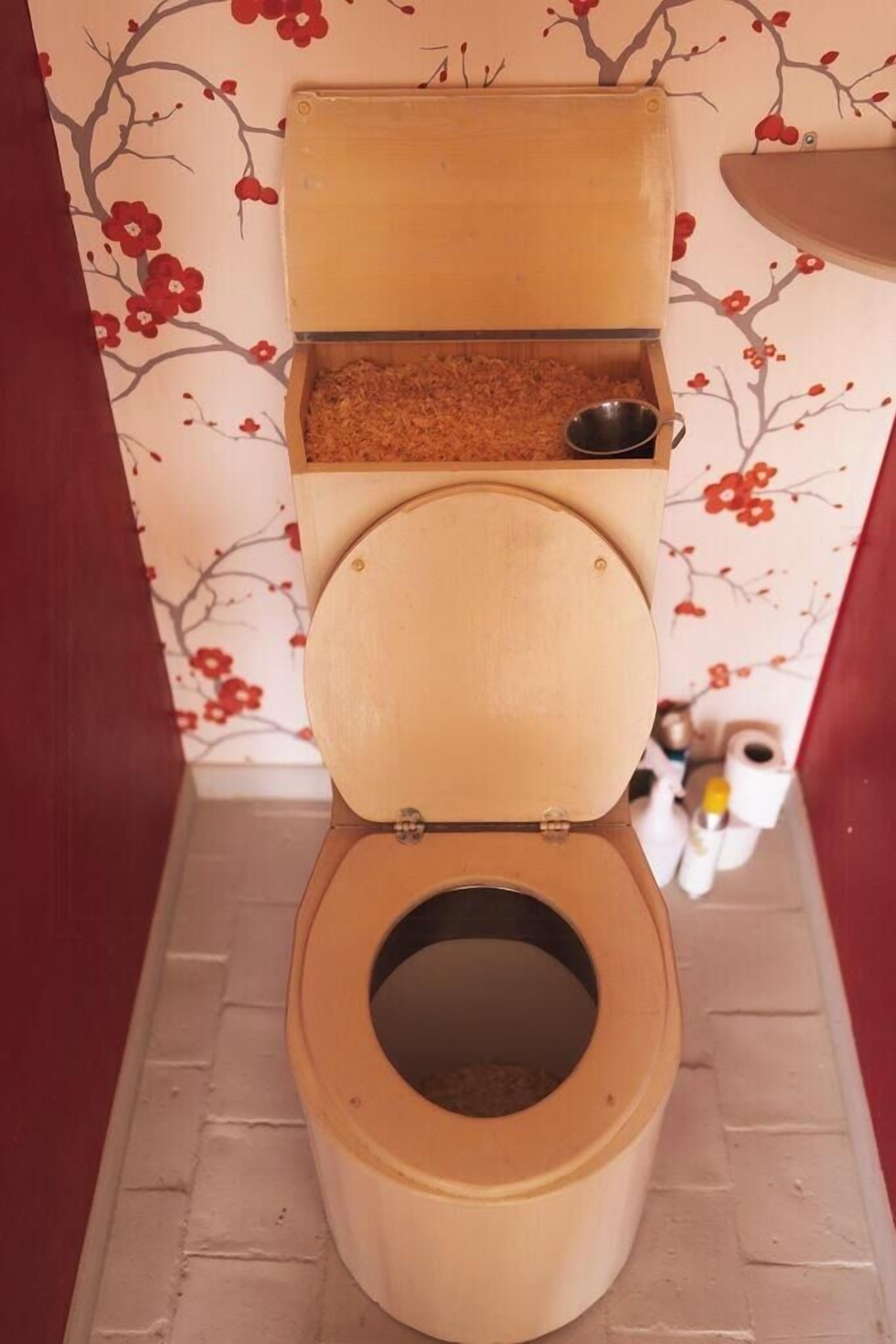 Eine Toilette mit Holzsitz und -deckel, einer Metallschüssel und einem Abfallbehälter.