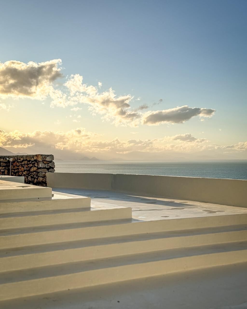 A seaside terrace with steps leading to a stone wall, overlooking the sea.