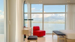 Una habitación de hotel moderna con un ventanal grande, una silla roja, un banco y un escritorio.