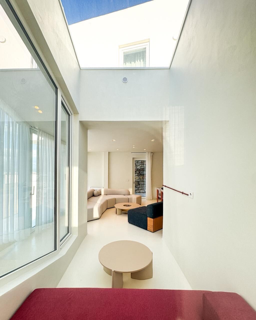 A modern interior with a glass wall, a round table, a sofa, and a stone wall in the background.