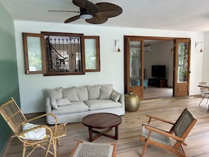 Ein Wohnzimmer mit einer Couch, zwei Korbstühlen, einem Couchtisch, einem Deckenventilator und einer großen Vase.