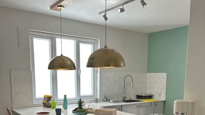 Eine moderne Küche mit einer zentralen Kochinsel, Barhocker, Pendelleuchten und Blick ins Freie.
