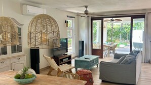 Ein großzügiger Wohnbereich mit einem Holzesstisch, Korbstühlen, einem grauen Sofa und einem Fernseher.