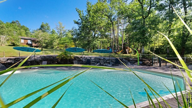 Ein klarer Pool mit Holzterrasse, umgeben von Bäumen und einem kleinen Gebäude im Hintergrund.