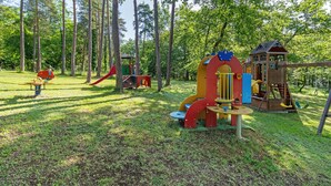 Ein Spielplatz mit verschiedenen Spielgeräten, umgeben von hohen Bäumen.