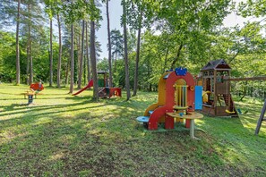 Ein Spielplatz mit verschiedenen Spielgeräten, umgeben von hohen Bäumen.