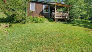 Eine kleine Holzhütte mit Veranda, umgeben von Gras und Bäumen.