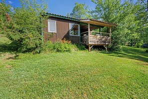 Eine kleine Holzhütte mit Veranda, umgeben von Gras und Bäumen.