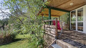 Ein überdachter Außenbereich mit Holzdeck, einem roten Stuhl und einem Holzzaun.