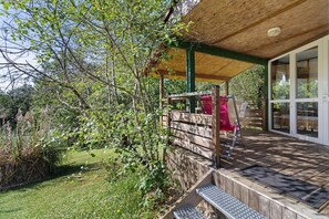 Ein überdachter Außenbereich mit Holzdeck, einem roten Stuhl und einem Holzzaun.