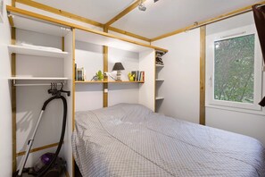 A compact room with a bed, built-in shelves, a window, and a vacuum cleaner. - Chalet 2 at Laupié near Sarlat (Proissans)