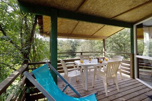 A covered outdoor area with a table and chairs, surrounded by wooden railings and greenery. - Chalet 2 at Laupié near Sarlat (Proissans)