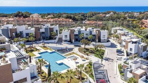 Una zona residencial moderna con piscina central, rodeada de edificios contemporáneos y vista al mar.