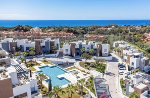 Ein modernes Wohngebiet mit einem zentral gelegenen Schwimmbad, umgeben von zeitgenössischer Architektur und Blick aufs Meer.