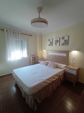 A bedroom with a bed, bedside tables, a nightstand, a ceiling fan, and wall art.
