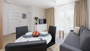 A modern living room with a sofa, dining table, and a TV. - Bright Apartment with Parking and Balcony | Close to the Airport (Warszawa)