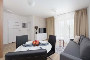 A modern living room with a sofa, dining table, and a TV. - Bright Apartment with Parking & Balcony Close to the Airport (Warszawa)