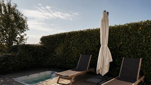 Eine Holzterrasse mit Whirlpool, zwei Liegestühlen und einem weißen Sonnenschirm.