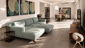 Ein modernes Wohnzimmer mit einer Eckcouch, einem Essbereich mit Tisch und Stühlen und Kunstwerken an den Wänden.