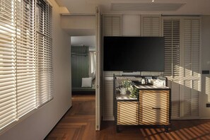 Une pièce avec une télévision, un meuble et une fenêtre avec des stores.