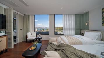 Habitación de hotel moderna con una cama grande, un área de descanso con una mesa y vista a una masa de agua.