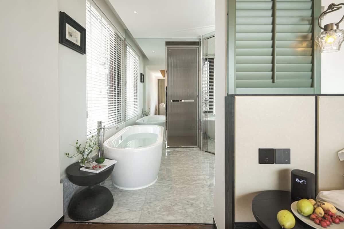 A modern bathroom with a freestanding bathtub, a round black side table, and a digital clock.