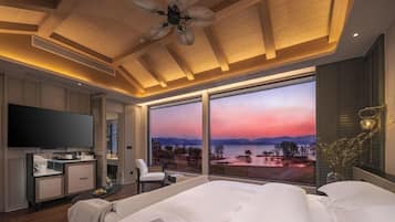 Een moderne hotelkamer met een groot bed, een flatscreen televisie, een bureau met stoel en uitzicht op een zonsondergang over het water.