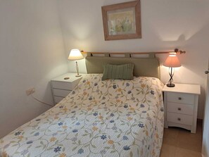 Une chambre à coucher avec un lit, deux tables de chevet, une commode, un oreiller vert, un tableau encadré au mur et une lampe sur chaque table de chevet.