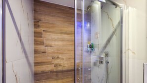 Zona de ducha con mampara de vidrio, suelo de madera y cabina de ducha de cristal.