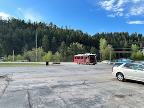 A parking lot with a red bus, a bench, and a white car. - The Old Style - Trolly Stop (Deadwood)