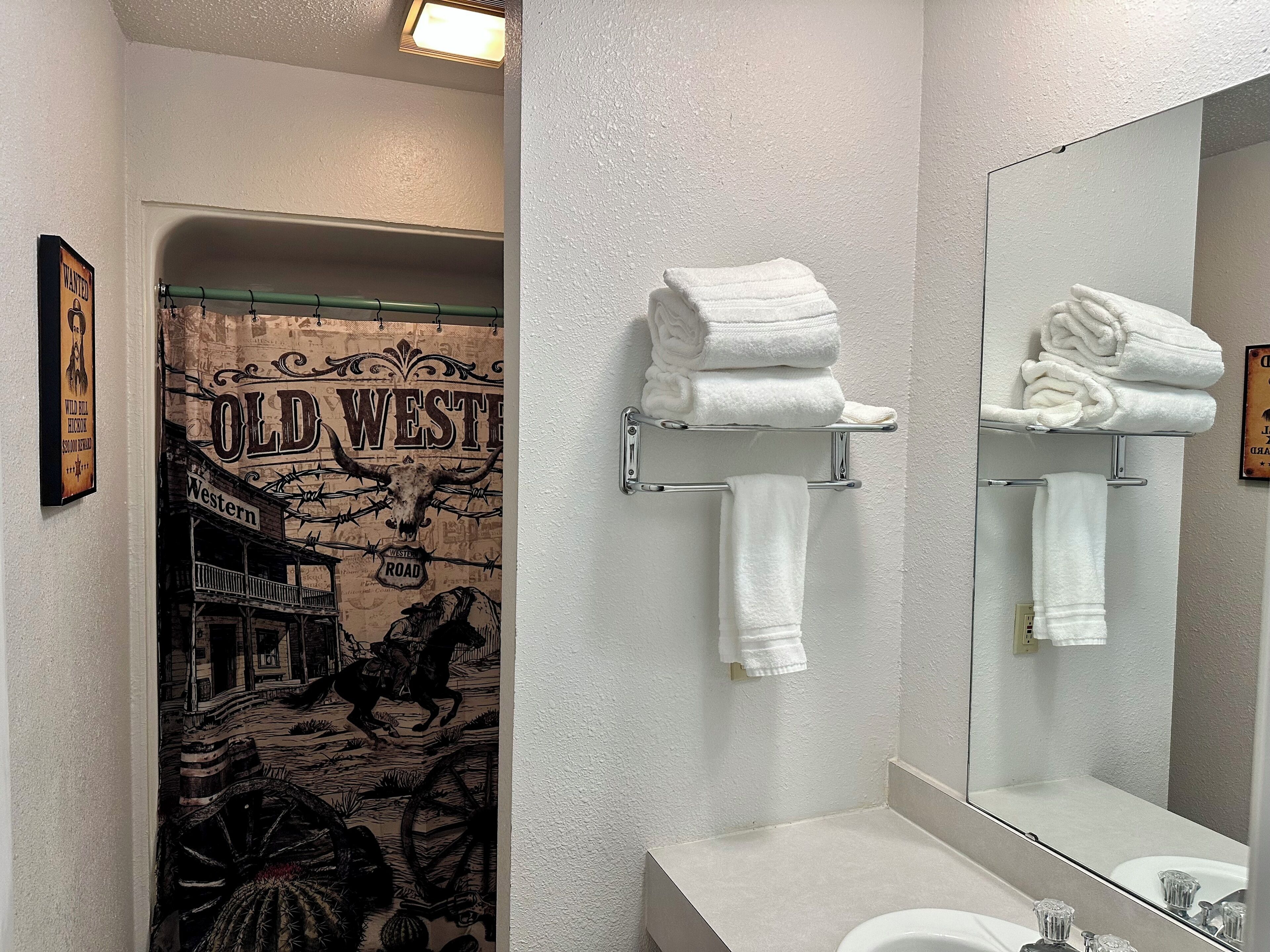 Une salle de bain avec un rideau de douche sur le thème du Far West, un miroir et deux porte-serviettes sur lesquels sont pliées des serviettes.