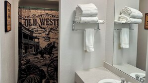 Une salle de bain avec un rideau de douche sur le thème du Far West, un miroir et deux porte-serviettes sur lesquels sont pliées des serviettes.