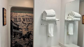 Une salle de bain avec un rideau de douche sur le thème du Far West, un miroir et deux porte-serviettes sur lesquels sont pliées des serviettes.