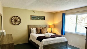 Une chambre à coucher avec un lit, une table de chevet, une lampe, une horloge murale et une fenêtre avec des rideaux.