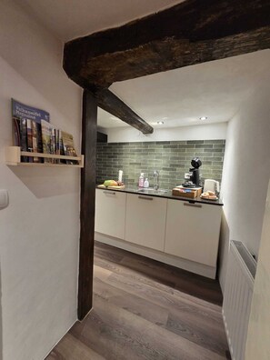 Eine moderne Küche mit einem dunklen Holzbalken, weißen Schränken, einer gefliesten Spritzschutzwand und einem kleinen Regal mit Zeitschriften.