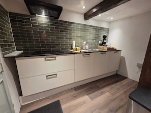 Eine moderne Küche mit dunkelgrüner Fliesenrückwand, weißen Schränken und Holzboden.