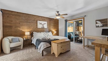 Une chambre avec un mur en bois, un lit avec une literie à motifs, une table de chevet, un banc en bois, un bureau et un ventilateur de plafond.