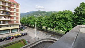 Ein mehrstöckiges Gebäude mit Balkonen, eine Straße mit parkenden Autos und ein grüner Hügel im Hintergrund.