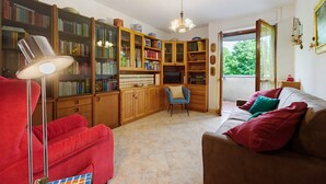 Ein Wohnzimmer mit einem roten Sessel, einem braunen Sofa, einem blauen Sessel, einer Stehlampe und einem Bücherregal voller Bücher.