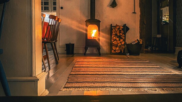 A cozy room with a wood-burning stove, a dining table with chairs, and a patterned rug on the floor. - Gorgeous and cosy 3-bedroom house in beautiful landscape. (Helsingborg)