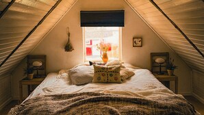 A bedroom with a sloped ceiling, a bed with a patterned blanket, a window with a view of the outside, and a small table with a lamp and a plant. - Gorgeous and cosy 3-bedroom house in beautiful landscape. (Helsingborg)