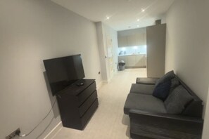 A living area with a TV, a sofa, and a kitchen in the background. - 1 Bedroom - Rubix (London)