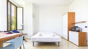 Una stanza piccola e pulita con un letto, una scrivania e angolo cottura.