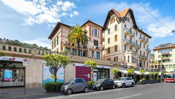 Una strada con auto parcheggiate, un edificio con balconi e una palma.