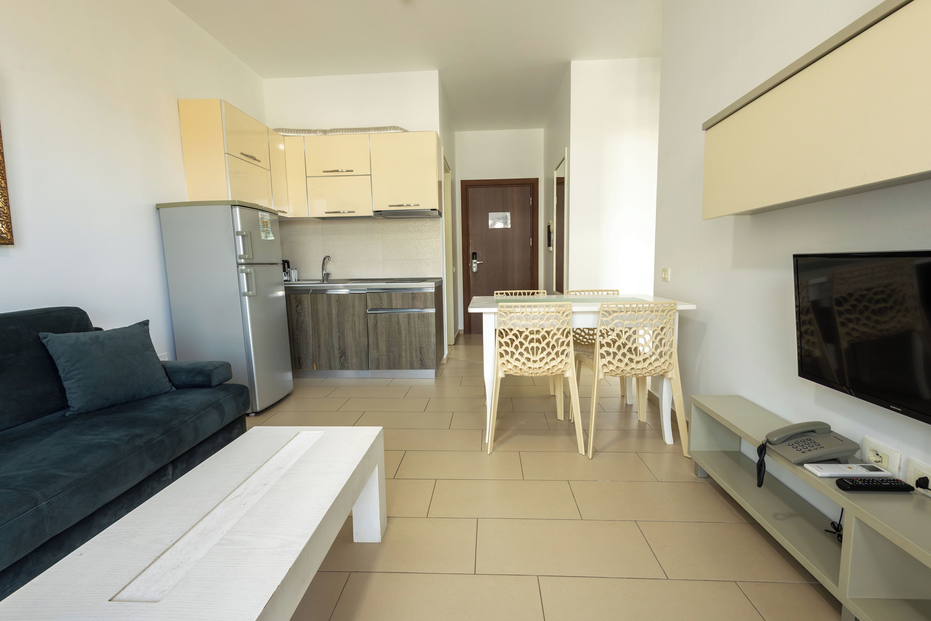 A compact living space with a kitchenette, a dining area, a sofa, a TV, and a phone.