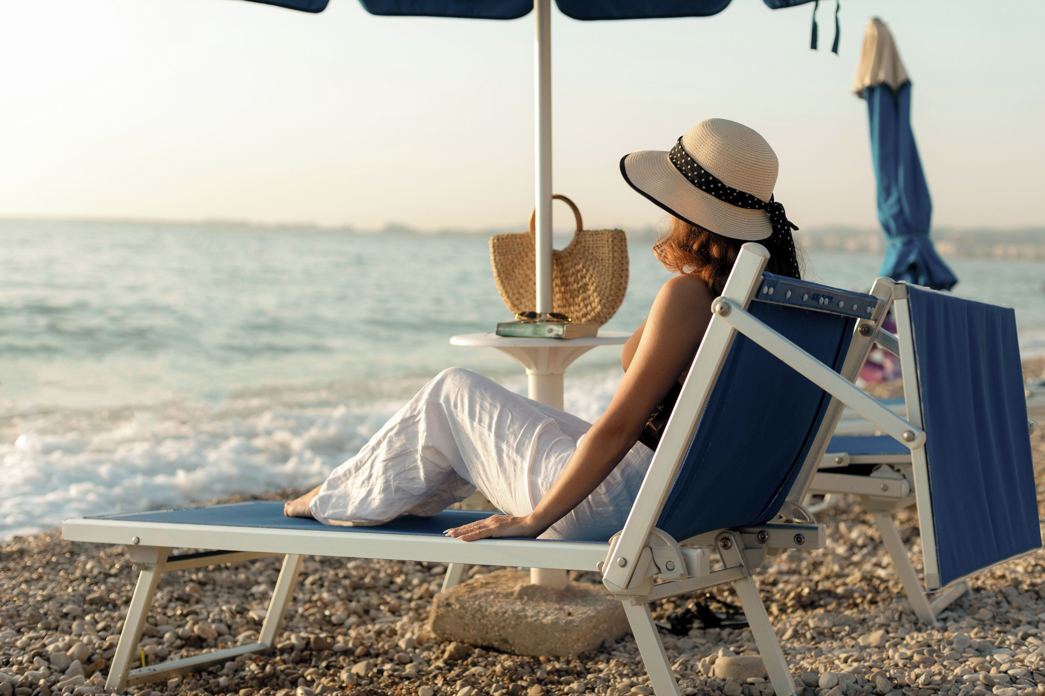 Une scène de plage avec une personne assise sur une chaise longue, un parasol de plage et une chaise de plage.