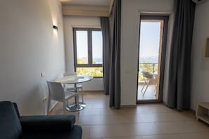 A modern living room with a sofa, a dining table with chairs, a balcony with a view, and a sliding door. - Britannia Resort & SPA (Vlorë)