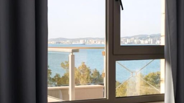 A room with a large window, a bed, and a view of a bridge and water. - Britannia Resort & SPA - All Inclusive (Vlorë)