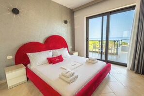 A hotel room with a large bed, a view of the sea, and a balcony with outdoor furniture.