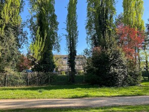 A park with tall trees, a building in the background, and a clear sky. - Au Fil du Clain - Cosy T2, parking & fiber (Poitiers)